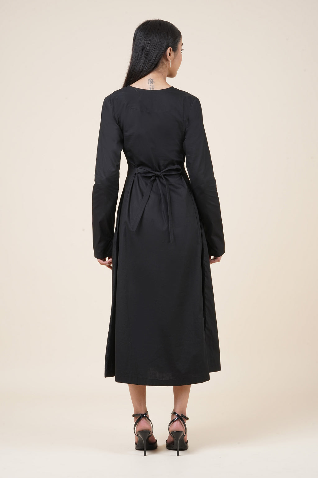 Woman wearing a black dress with a belt on a beige background