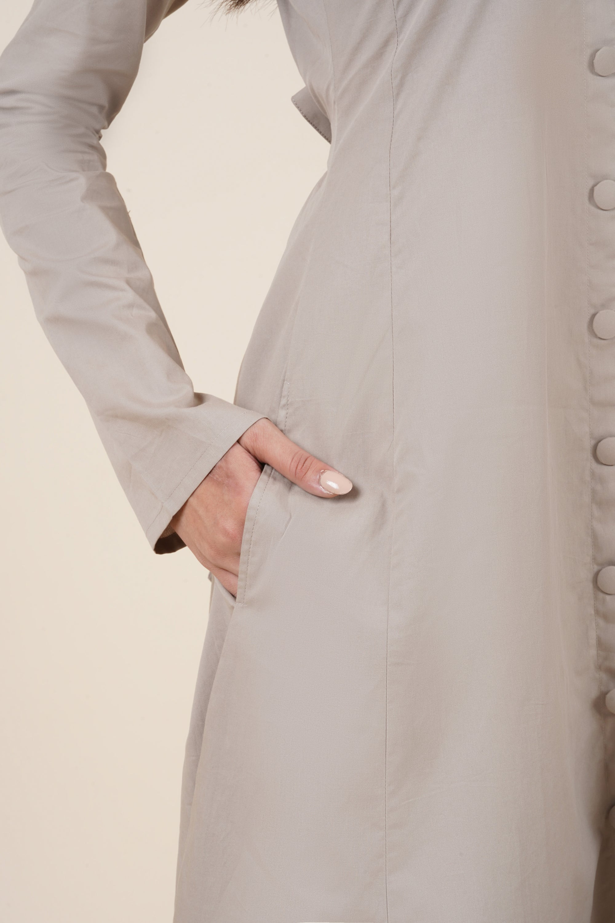Close-up of a person wearing a beige coat with button details on a neutral background