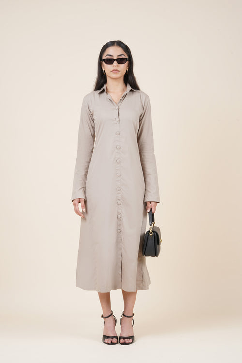 Woman wearing a beige button-up dress with sunglasses and a black handbag on a plain background