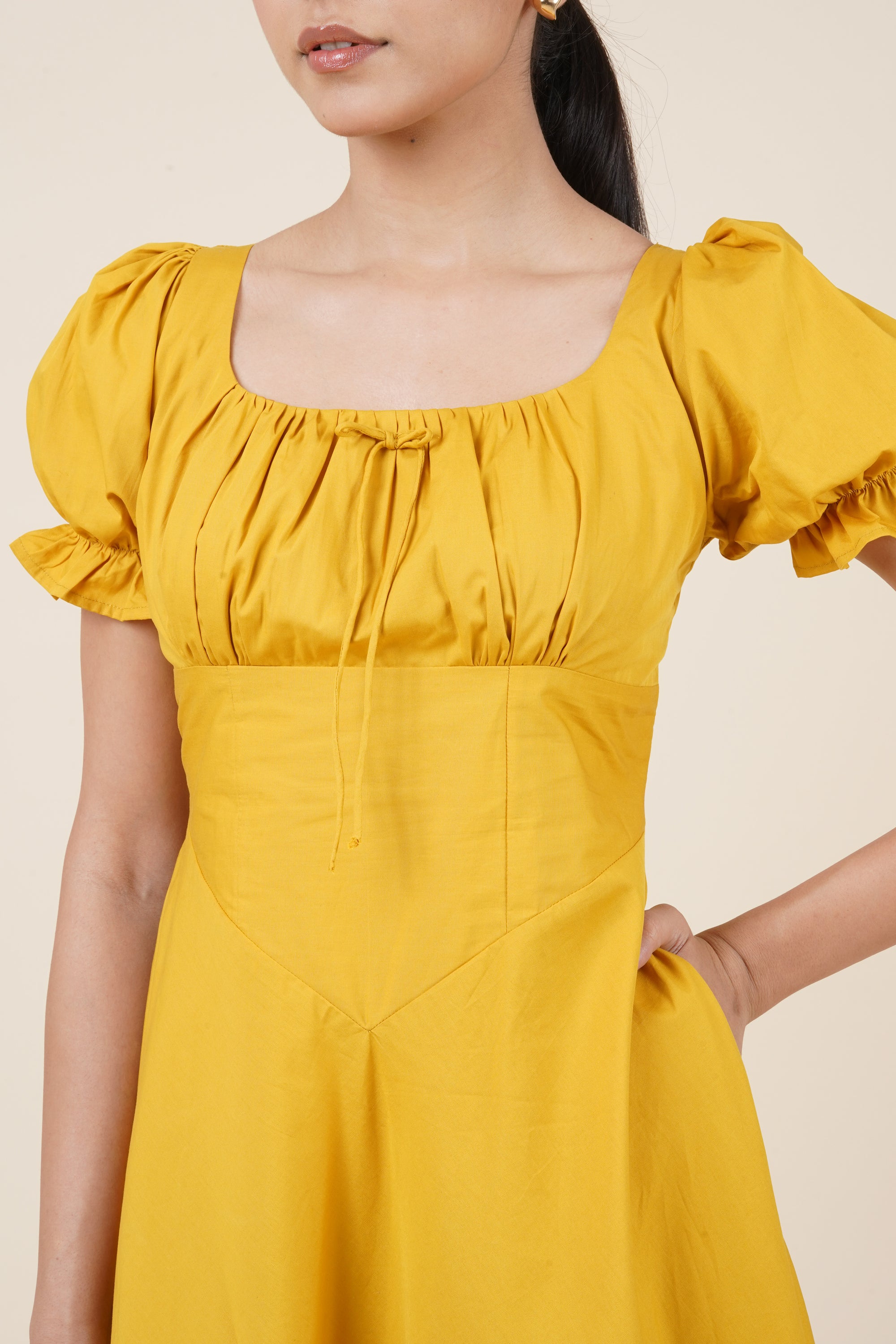 Yellow dress with puff sleeves worn by a person on a beige background