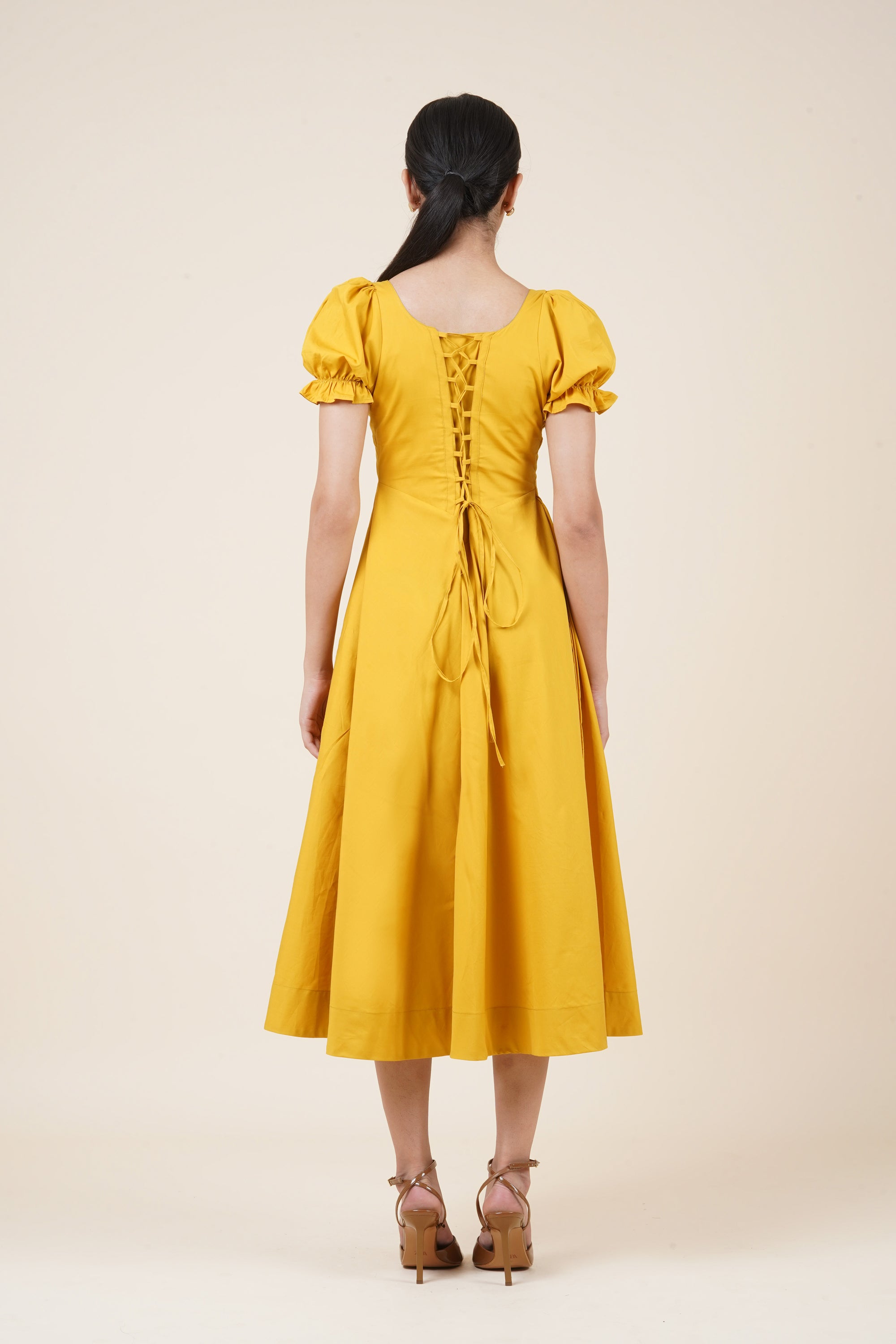 Yellow dress with puff sleeves and a button detail on a beige background