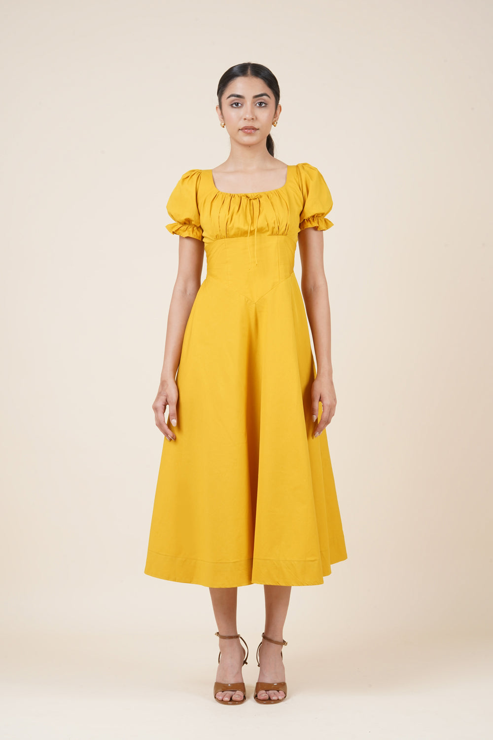 Woman wearing a yellow dress with puff sleeves on a beige background