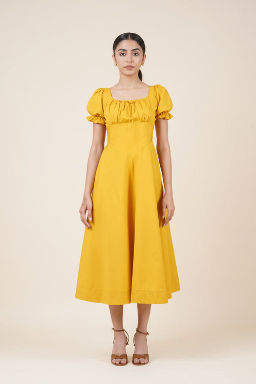 Woman wearing a yellow dress with puff sleeves on a beige background